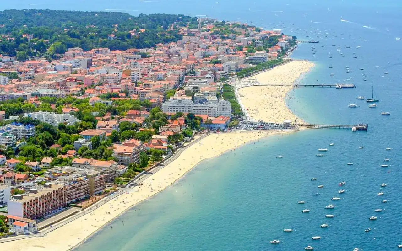 Vue aérienne d'une ville côtière avec une plage bondée et des bateaux dans l'eau.