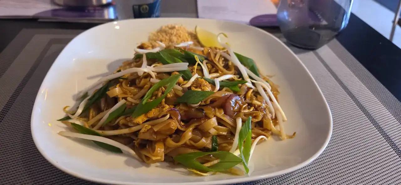 Pad thai z kurczakiem, kiełkami fasoli mung, szczypiorkiem i ćwiartką limonki na białym talerzu.