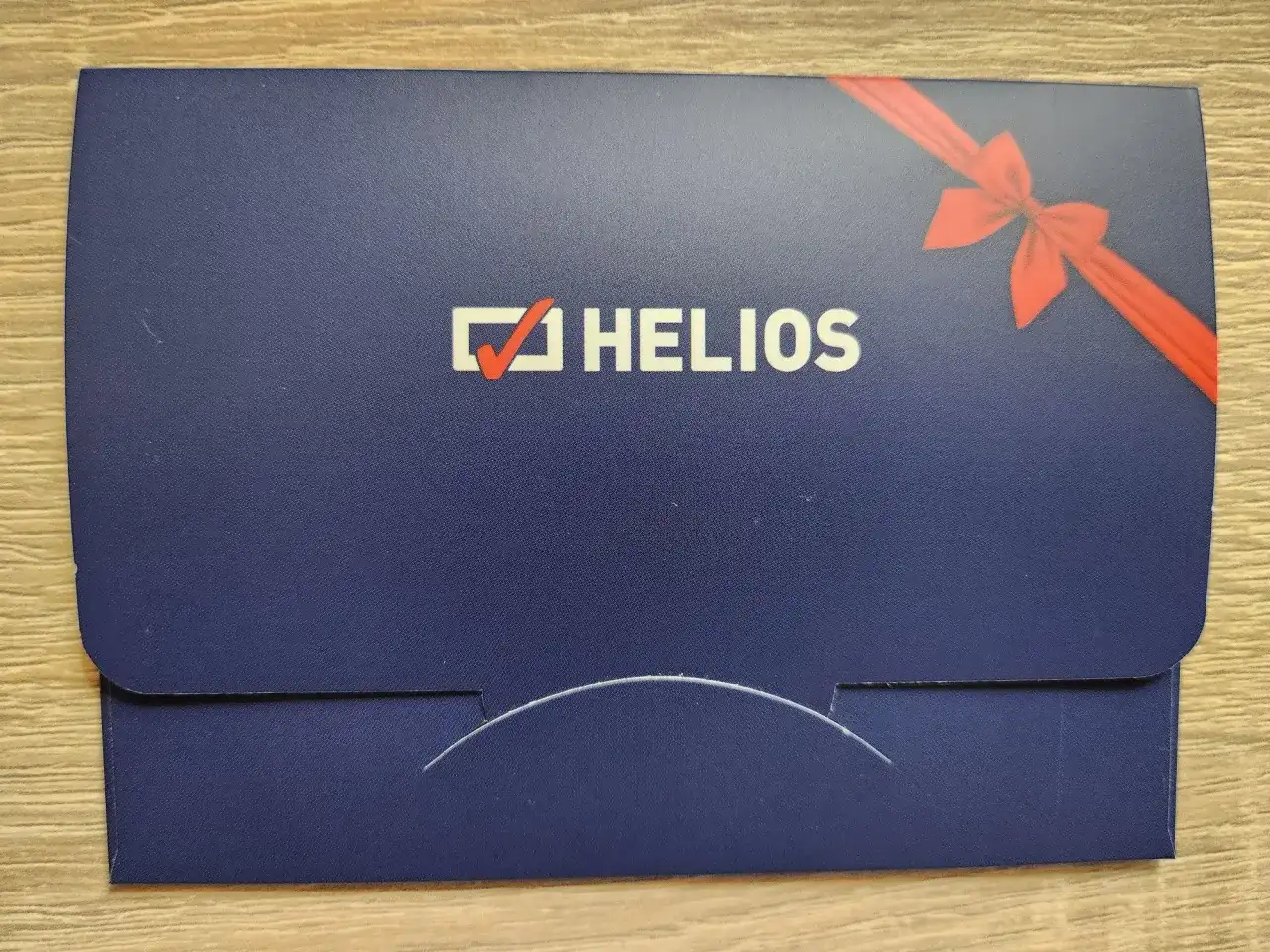 Chcesz wiedzieć, ile kosztuje voucher do kina Helios? Na zdjęciu widać elegancką, granatową kopertę z logo Helios i czerwoną wstążką, idealną na prezent.