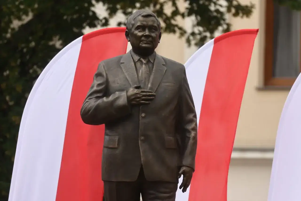 Pomnik Lecha Kaczyńskiego, jednego z wielu w Polsce, stoi na tle biało-czerwonych flag.