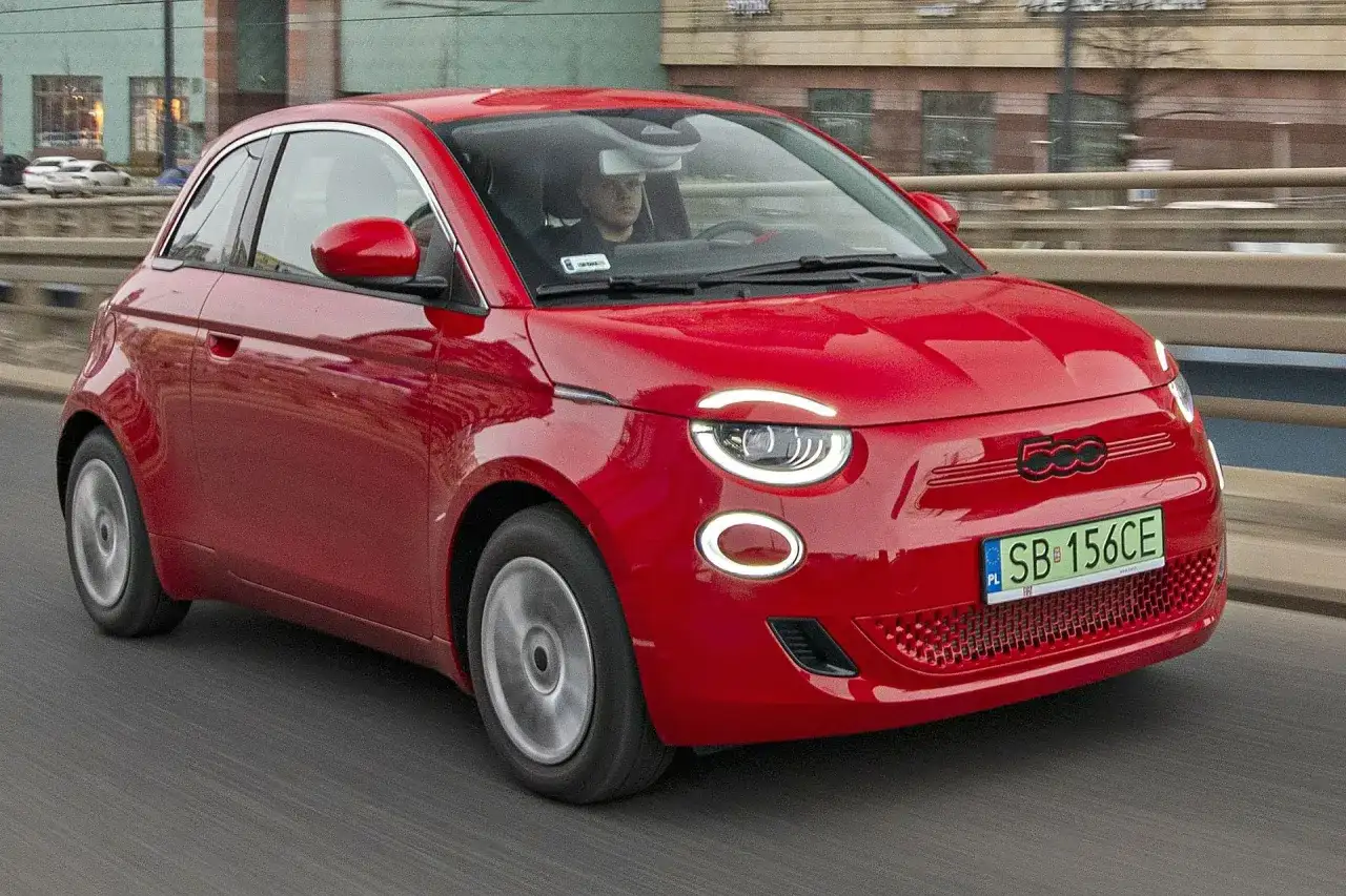 Czerwony Fiat 500 jedzie po drodze. Sprawdź aktualną fiat 500 cena i dowiedz się więcej o tym stylowym samochodzie.