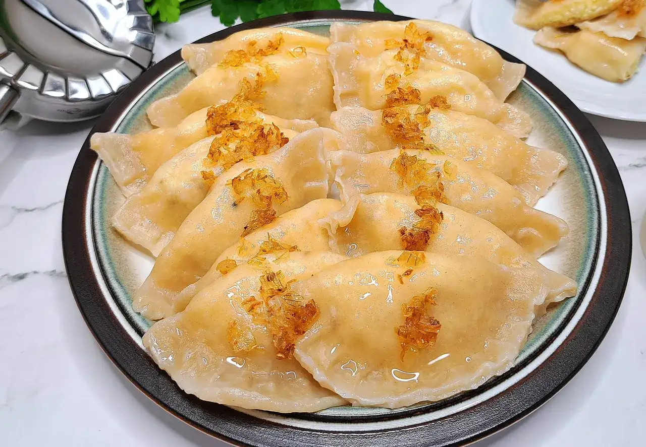 Talerz pełen pysznych pierogów ruskich, polanych tłuszczem i posypanych skwarkami. Idealne, by pokazać, jak zrobić pierogi ruskie.