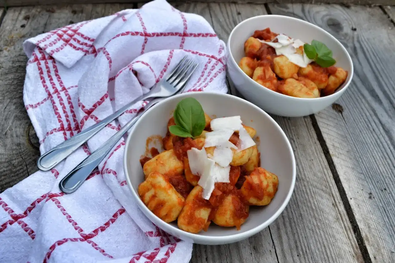 Dwa talerze pysznych gnocchi z sosem pomidorowym, posypane parmezanem i udekorowane bazylią, gotowe do podania.