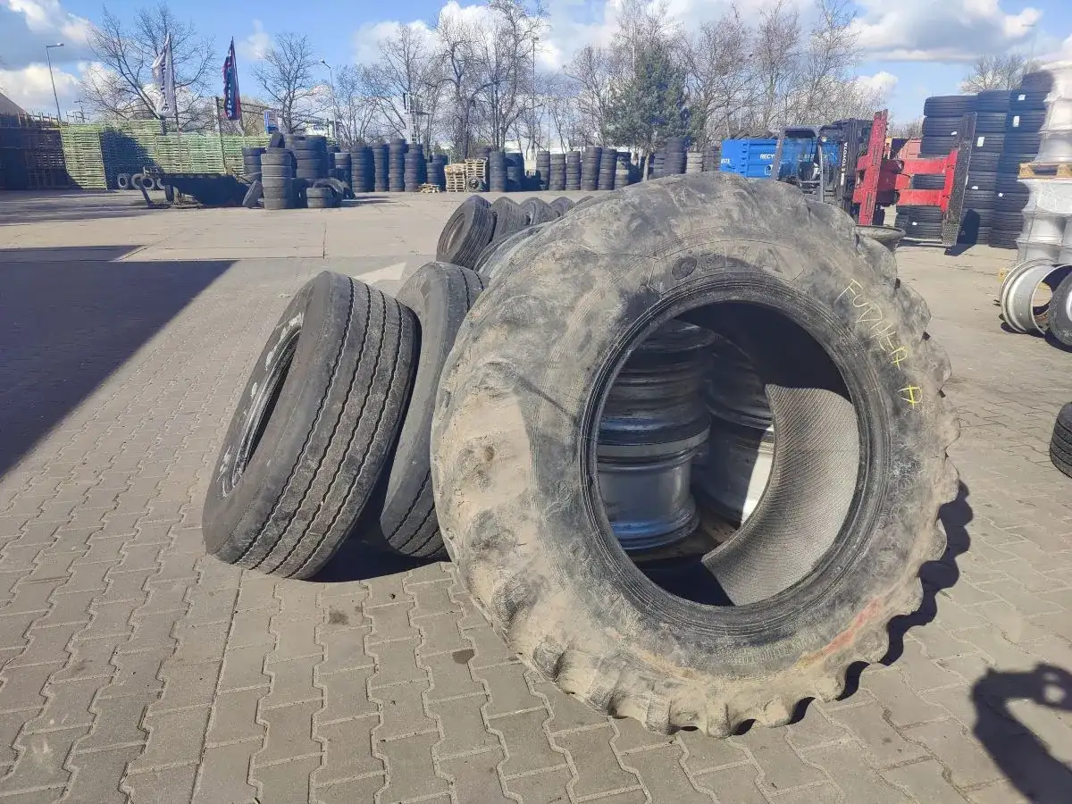 Duże opony rolnicze i samochodowe czekają na recykling opon. W tle widać stosy opon i sprzęt.