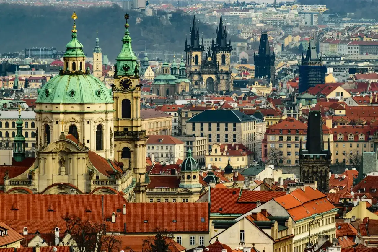 Widok panoramy Pragi z charakterystycznymi wieżami i zielonymi kopułami.
