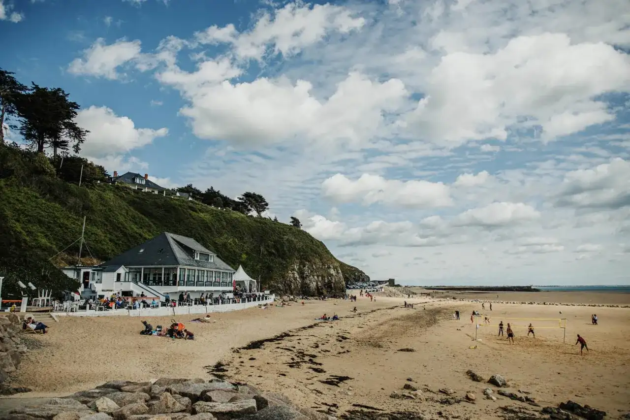 Plage normande avec restaurant en bord de mer, gens sur le sable et terrain de volley.