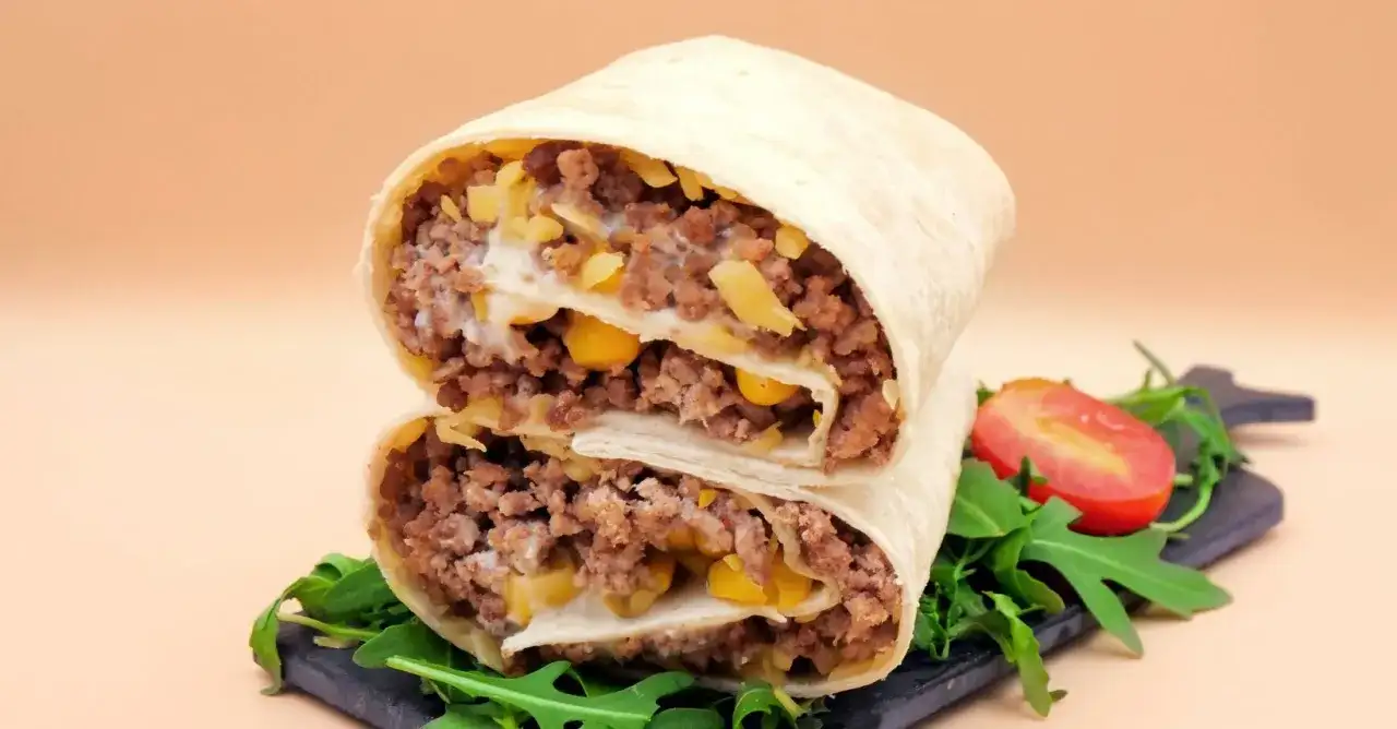 Pyszna tortilla z mięsem mielonym, kukurydzą i serem, przekrojona na pół, z rukolą i pomidorkiem.