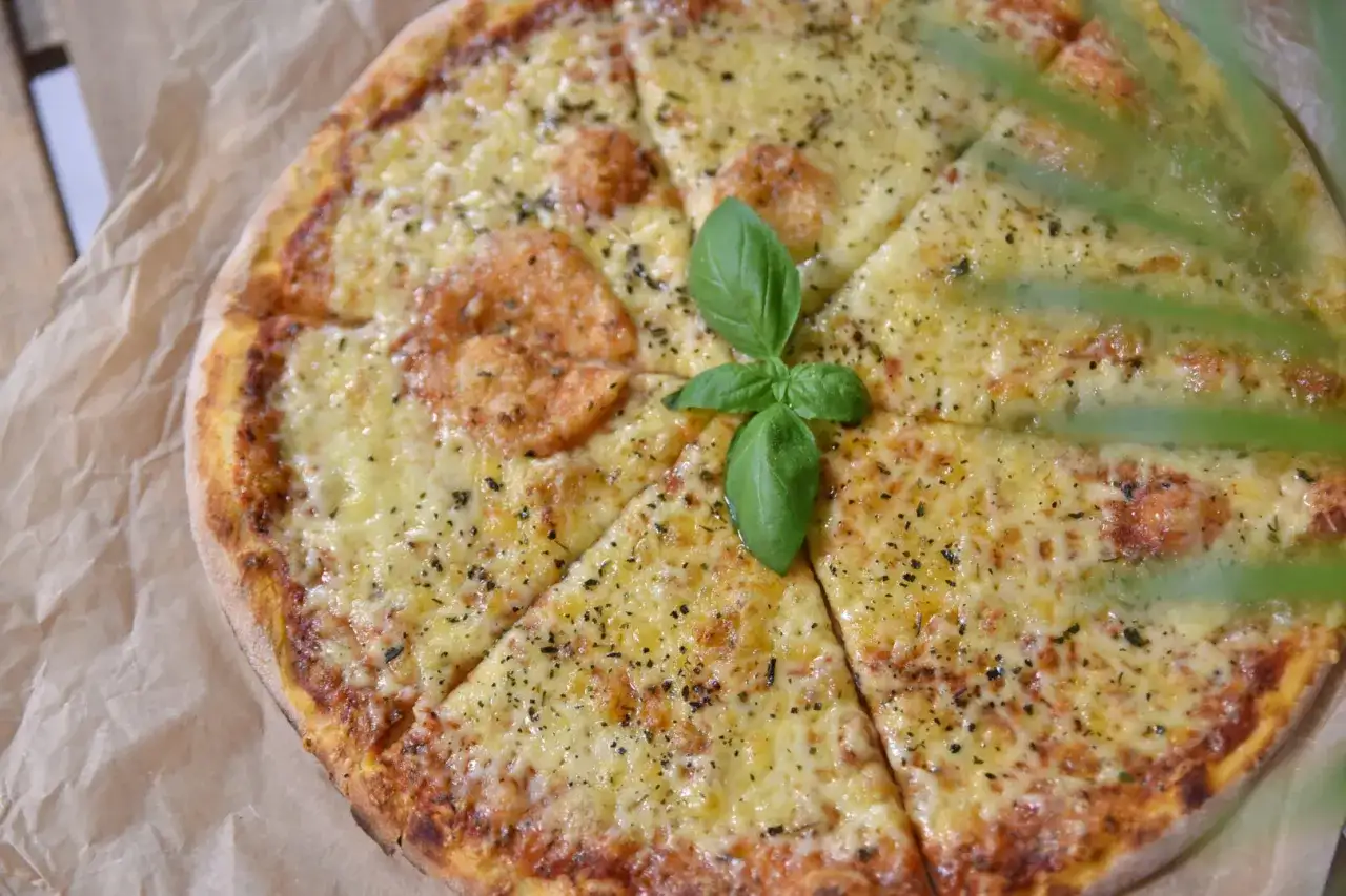 Pyszna pizza z roztopionym serem, posypana ziołami i udekorowana listkiem bazylii. Idealny ser do pizzy dla każdego smakosza.