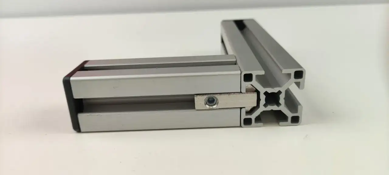 Dwa połączone profile aluminiowe konstrukcyjne tworzą kąt prosty. Widać element łączący z nakrętką.