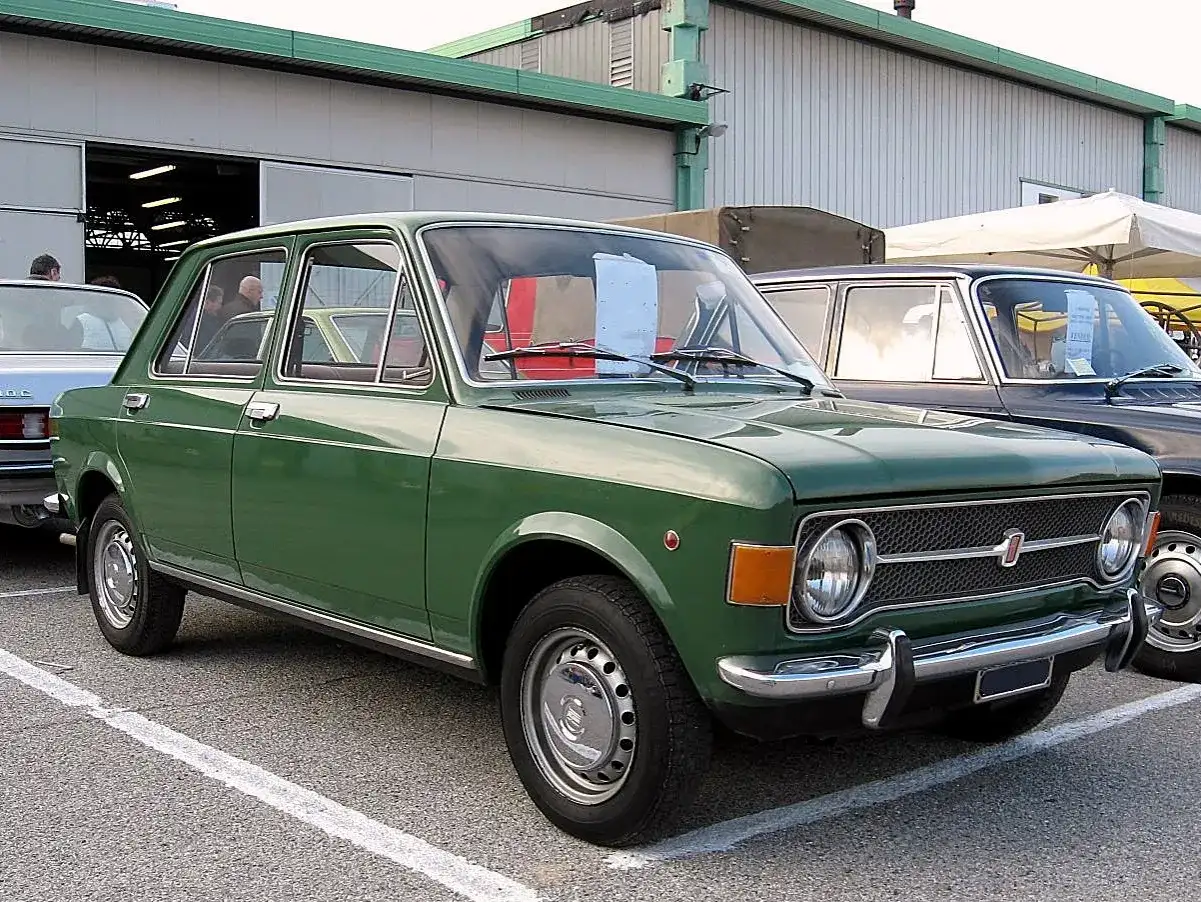 Zielony fiat 128, klasyk z lat 70., zaparkowany przed budynkiem.