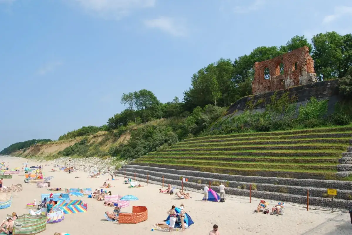 Plaża w Rewalu z ruinami na klifie. Ludzie odpoczywają na piasku, ciesząc się słońcem i widokiem. To popularne rewal atrakcje.