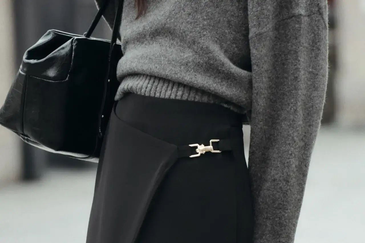 Chaqueta gris y bolso negro sobre falda negra larga con detalle dorado. Un look elegante para saber como combinar una falda negra larga.