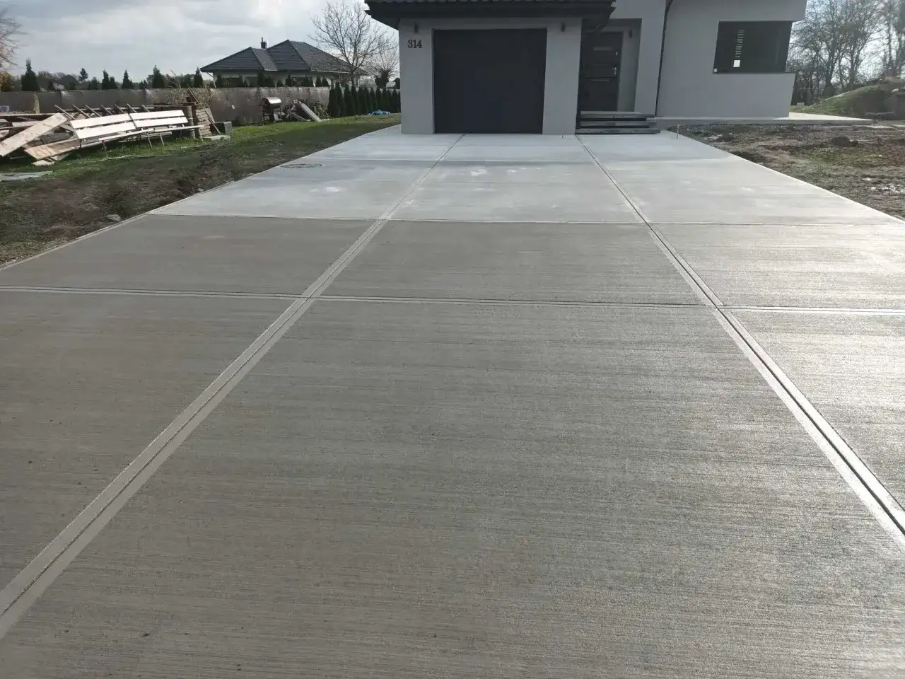 Nowy podjazd z beton stemplowany, z wyraźnymi fugami, prowadzi do nowoczesnego domu z szarą bramą garażową.