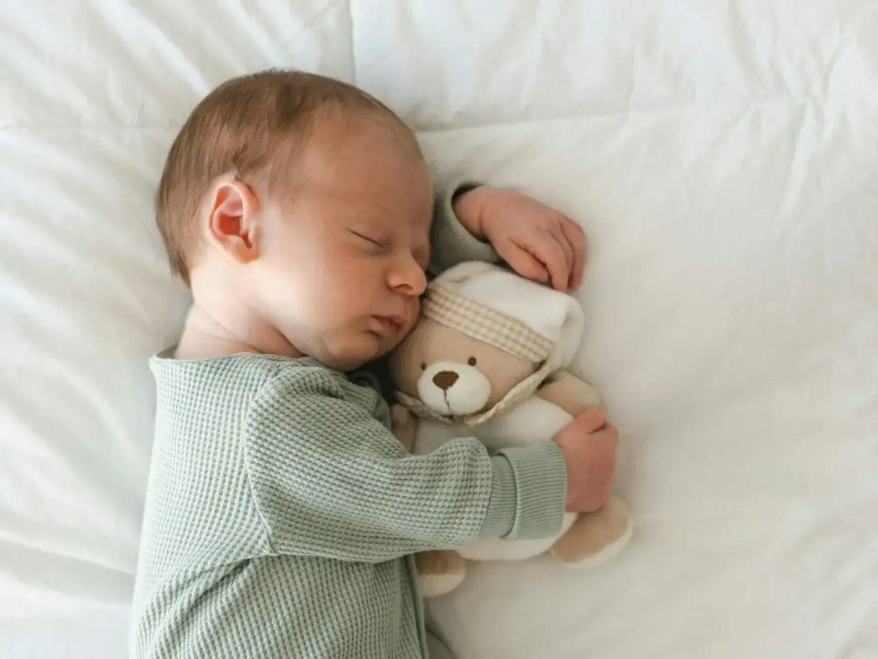 Śpiące niemowlę tuli misia. Wkrótce odkryje świat dzięki kolorowym książeczkom sensorycznym.