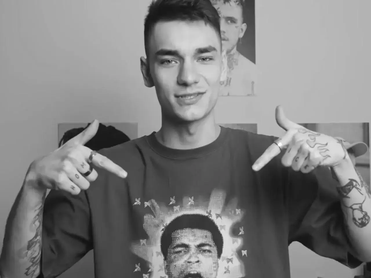 Młody youtuber w koszulce z Muhammadem Alim, z tatuażami na rękach, wskazuje na siebie.