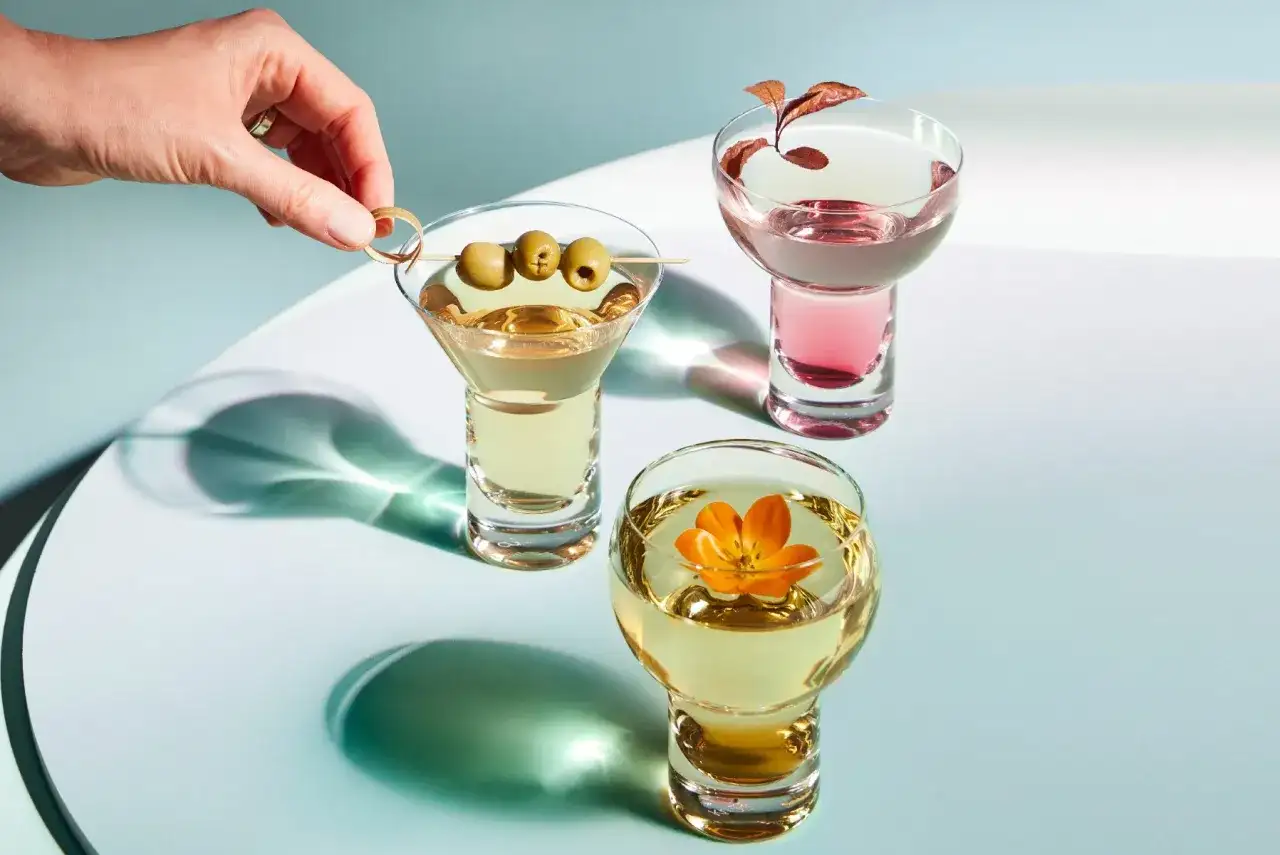 Trzy drinki z wódką: jeden z oliwkami, drugi z kwiatem, trzeci z gałązką.