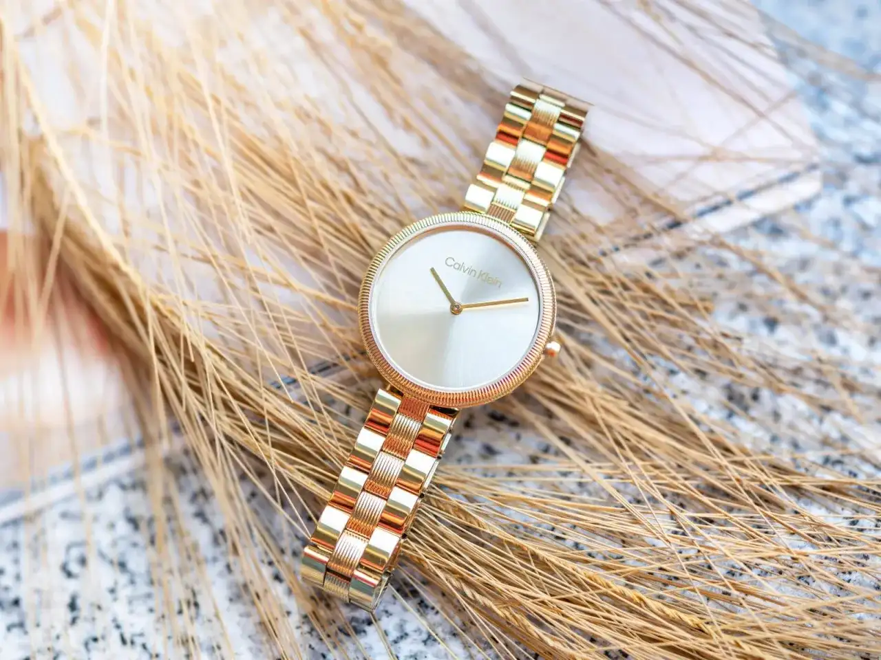 Złoty zegarek damski Calvin Klein na tle kłosów.