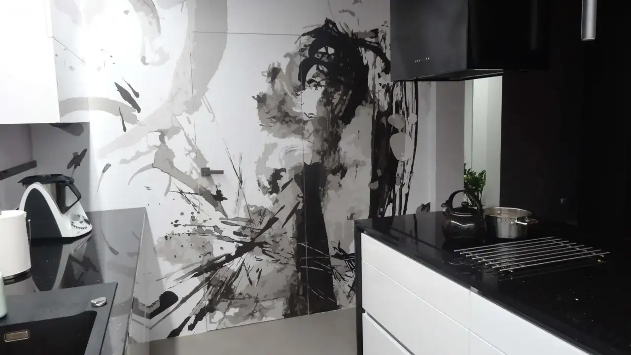 Nowoczesna kuchnia z czarnym blatem i białymi szafkami. Na ścianie artystyczny mural, który świetnie maskuje drzwi.