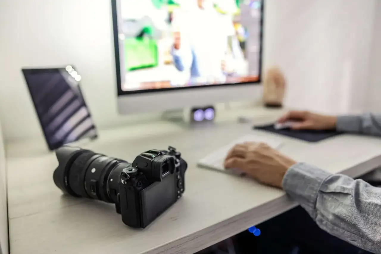 Aparat Sony leży obok komputera, gotowy do zgrania zdjęć. Na ekranie widać edytowane obrazy, a dłonie pracują przy klawiaturze.