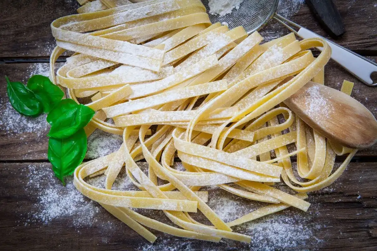 Świeży makaron tagliatelle, posypany mąką, z listkami bazylii. Idealny jako alternatywa, czym zastąpić makaron pszenny.