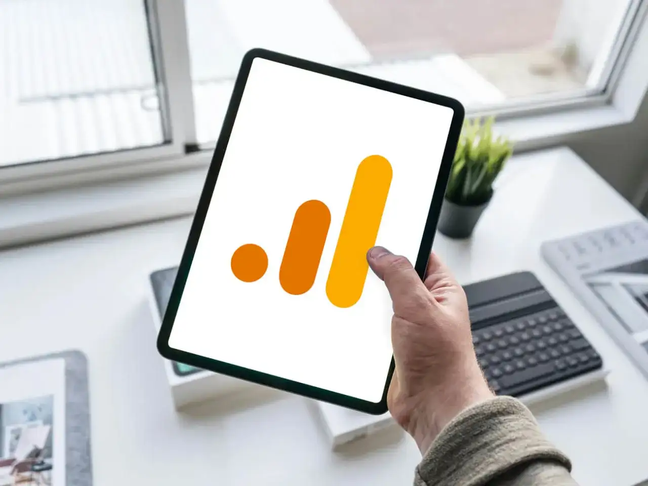 Ręka trzyma tablet z ikoną Google Analytics 4. Analiza zdarzeń GA4 na urządzeniu mobilnym.