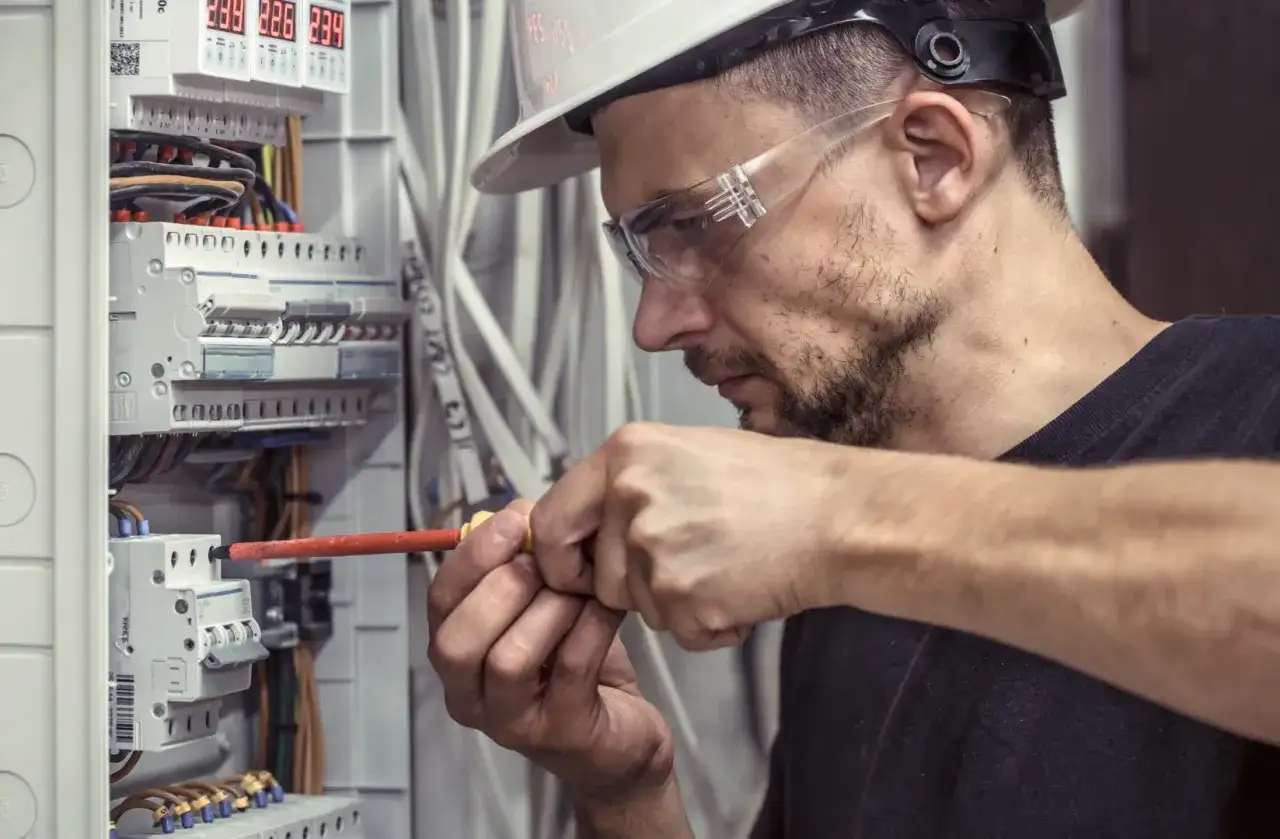 Technik elektryk w okularach ochronnych i kasku precyzyjnie dokręca śrubę w skrzynce rozdzielczej.