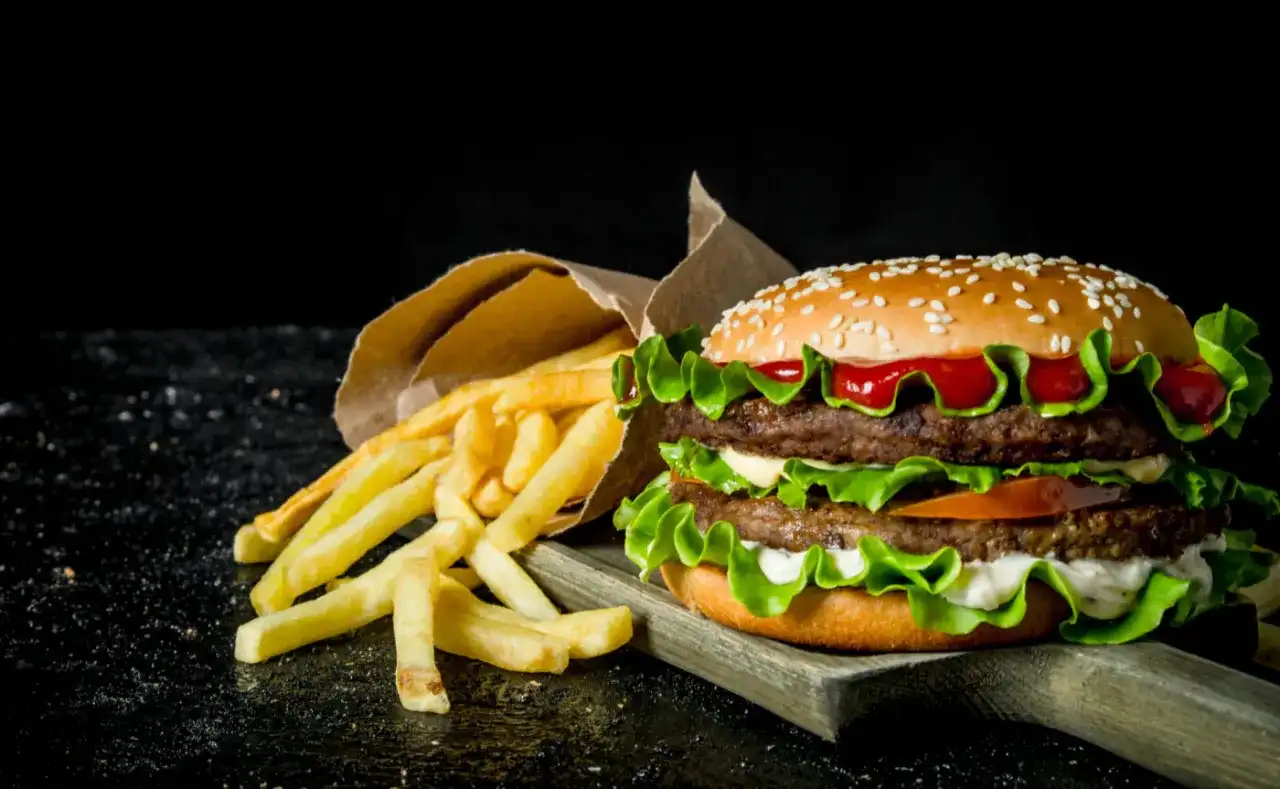 Podwójny hamburger z frytkami na ciemnym tle.