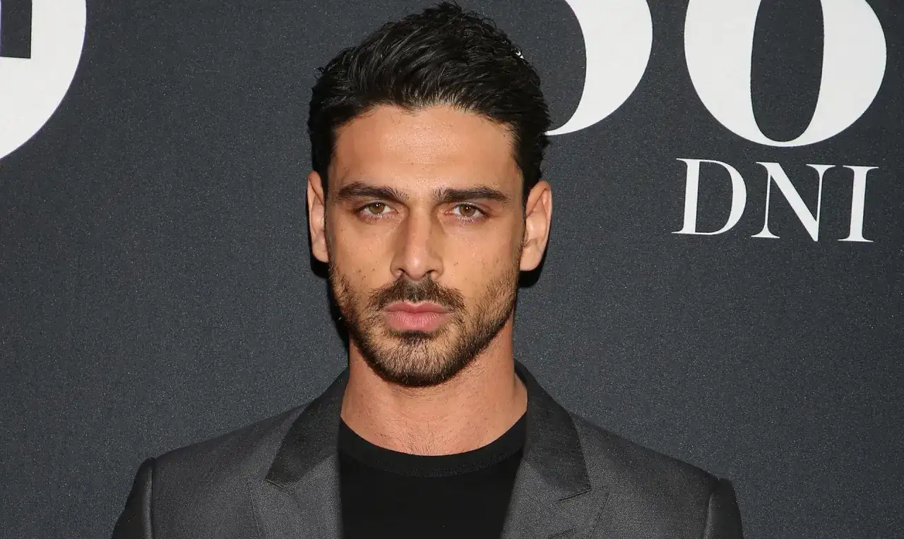 Michele Morrone w szarej marynarce i czarnej koszulce na tle napisu "DNI".