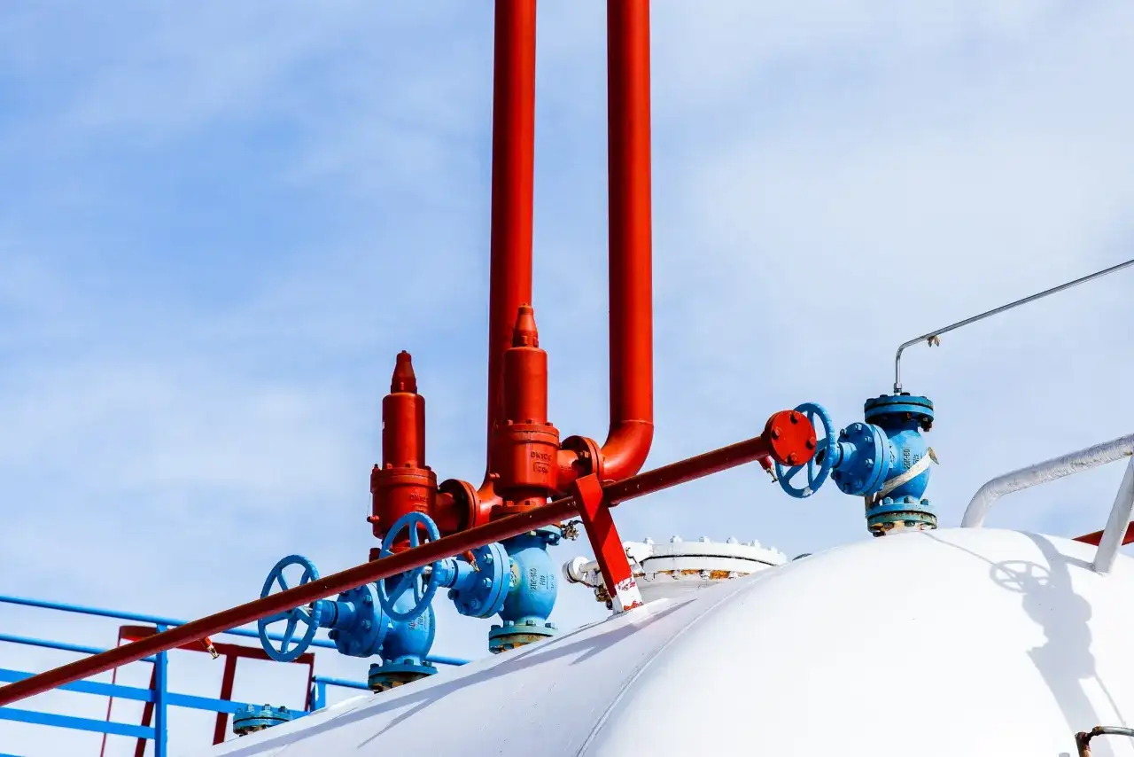 Czerwone i niebieskie zawory na białym zbiorniku na gaz. Zastanawiasz się, na ile wystarcza zbiornik na gaz 2700?