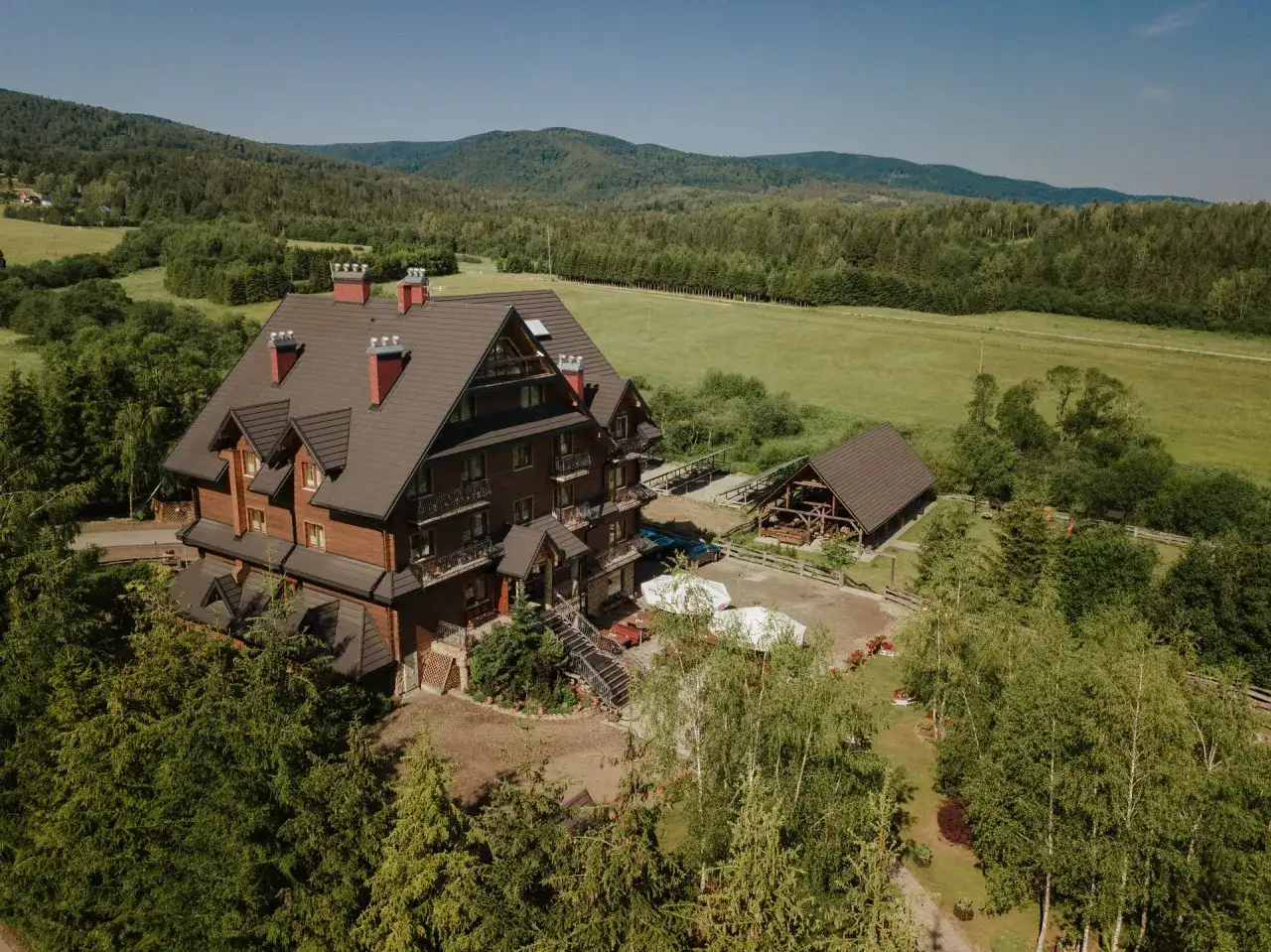 Hotel Carpatia Bieszczadzki Gościniec w otoczeniu zieleni, z drewnianym budynkiem i widokiem na góry.