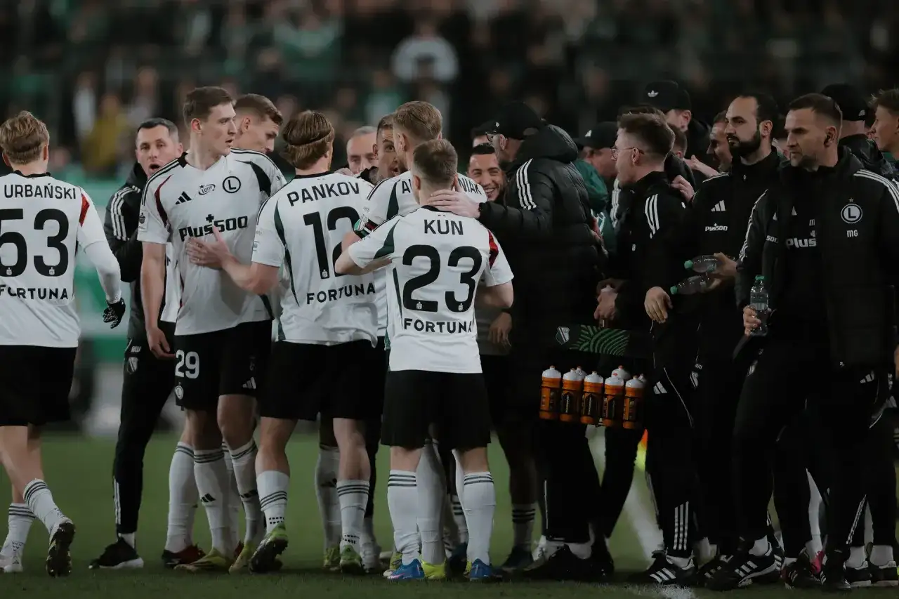 Legia Warszawa zawodnicy w białych strojach świętują na boisku. Widać numery 53, 29, 12 i 23.