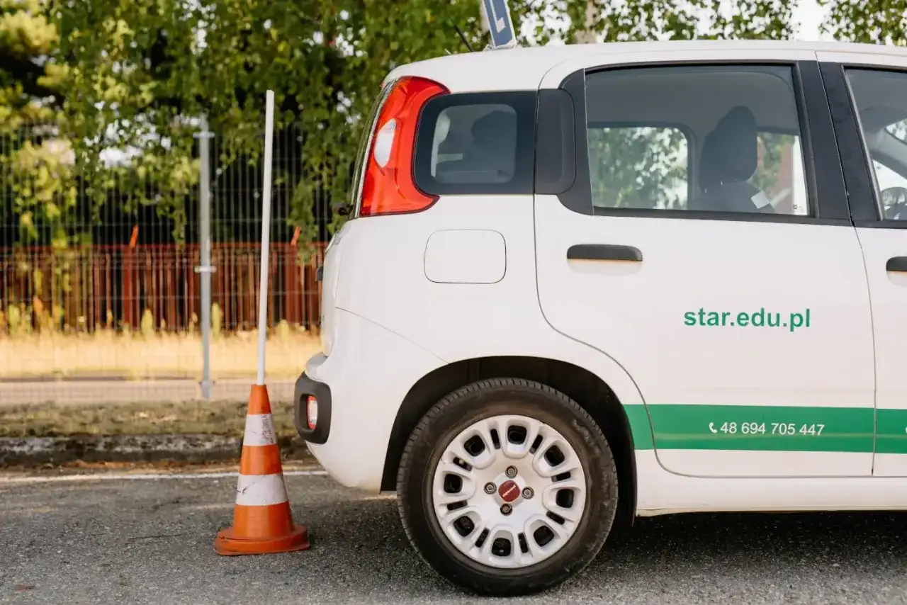 Biały samochód szkoleniowy z pachołkiem obok. Zastanawiasz się, ile kosztuje prawo jazdy w Polsce?