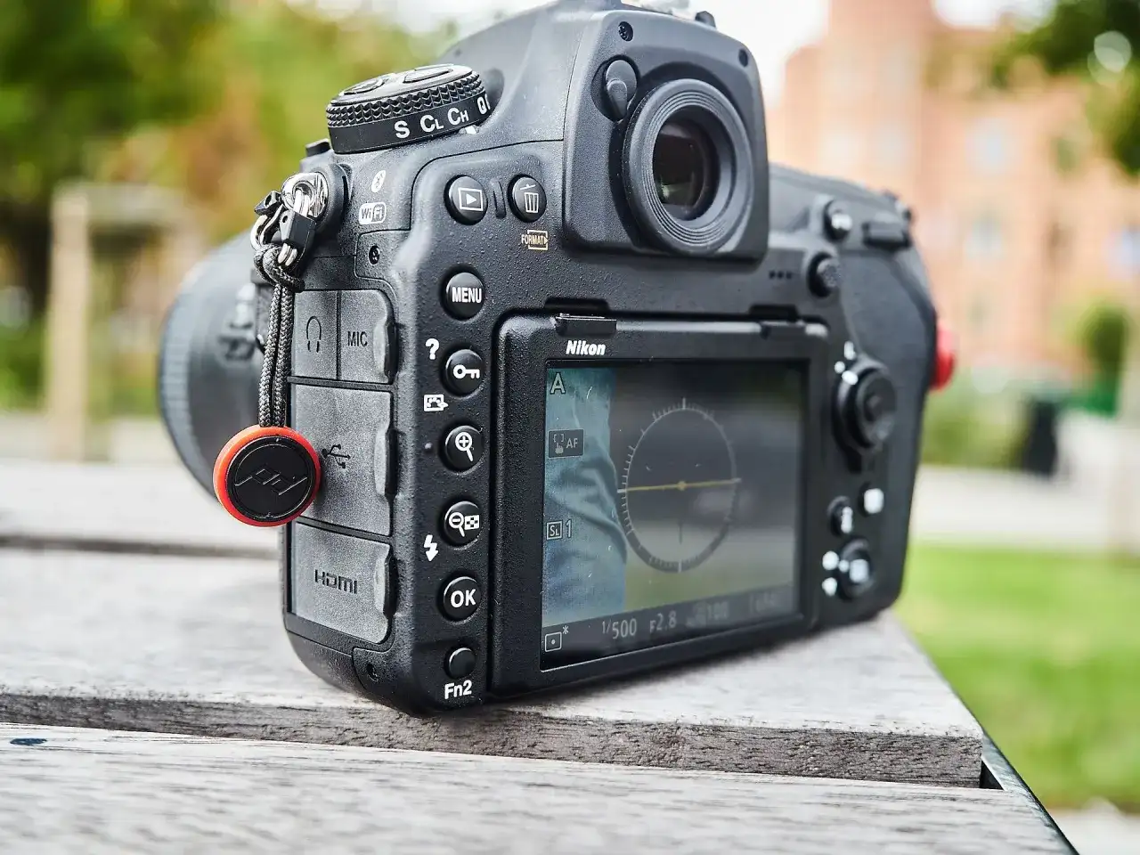 Nikon D850 test w plenerze. Aparat leży na drewnianym stole, w tle zieleń i budynek.