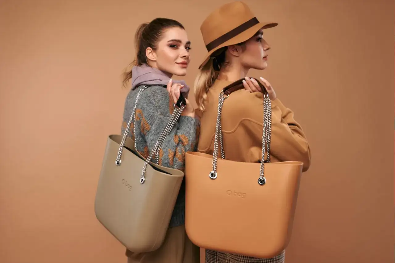 Dwie kobiety prezentują modne torebki na lato. Jedna w beżowym swetrze, druga w brązowym kapeluszu.
