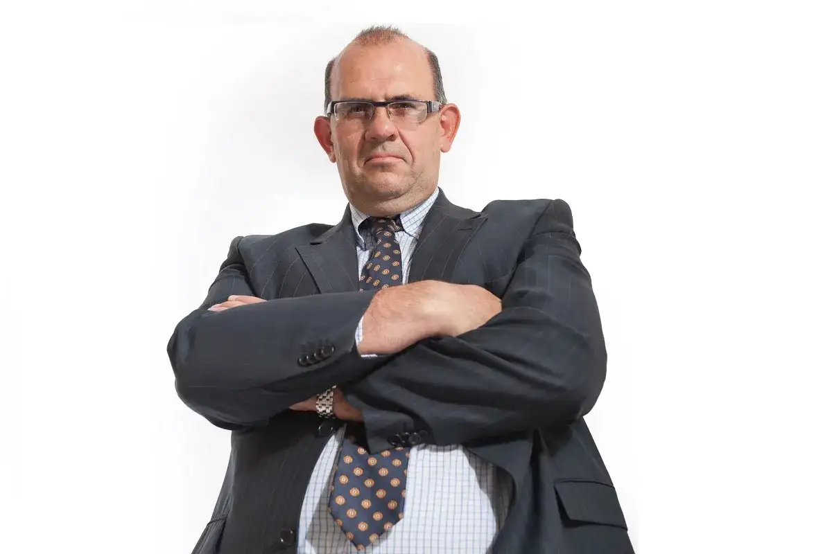 Mężczyzna w garniturze i okularach ze skrzyżowanymi ramionami, patrzący na wprost.