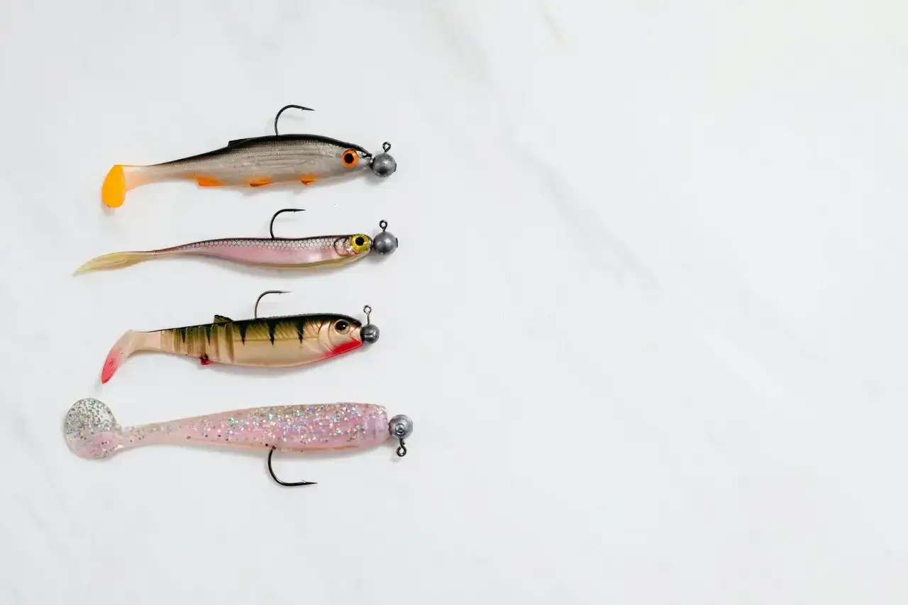 Cztery gumowe przynęty wędkarskie w kształcie rybek na białym tle.