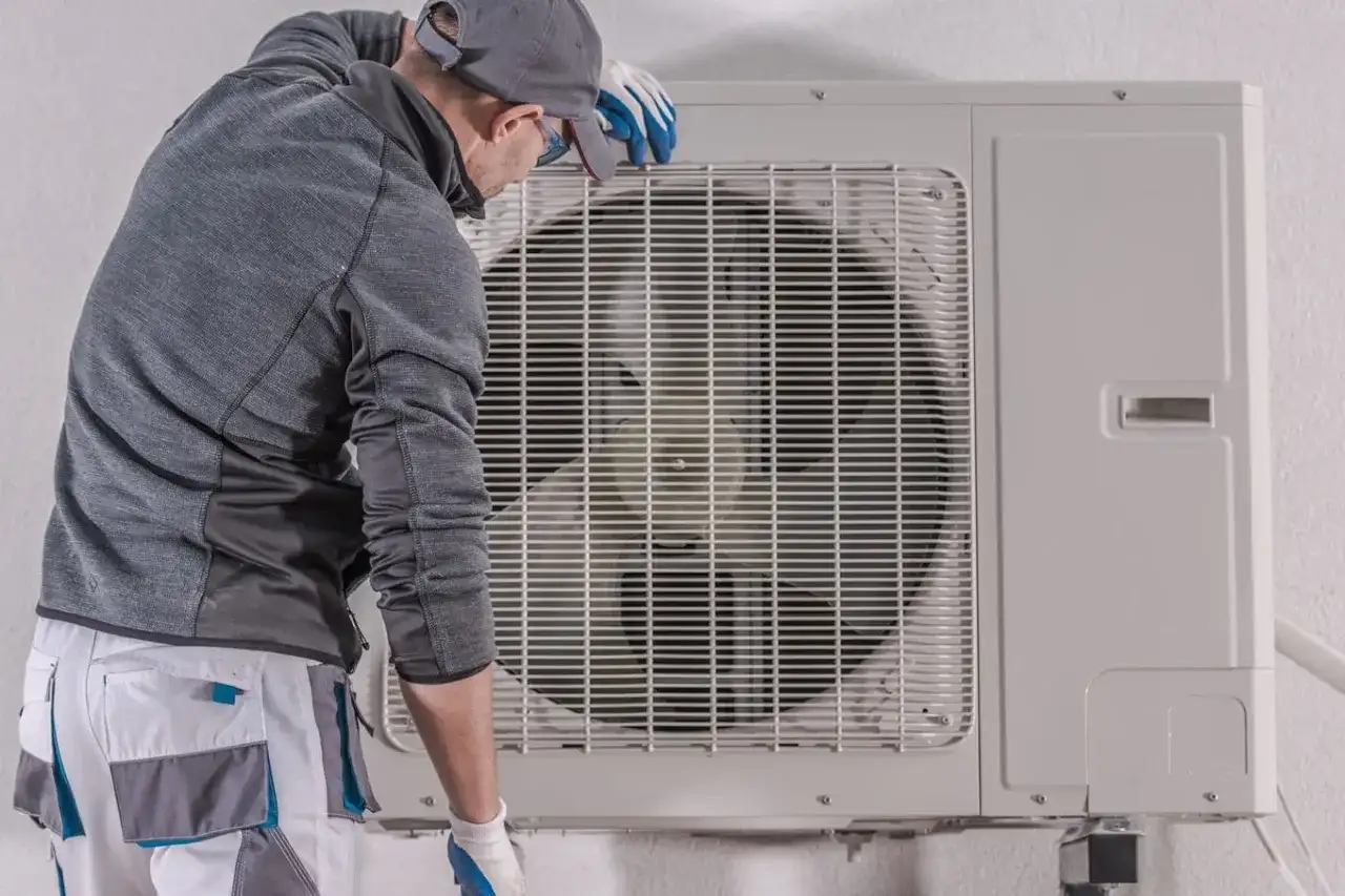 Technik w rękawiczkach sprawdza jednostkę zewnętrzną pompy ciepła, być może w celu diagnozy awarii pomp ciepła.