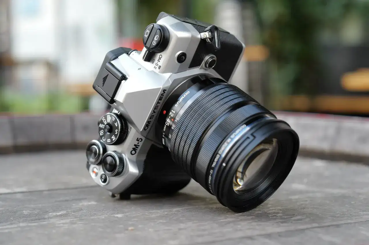 Srebrny aparat OM SYSTEM OM-5 z obiektywem M.ZUIKO DIGITAL 12-45mm 1:4, gotowy do uchwycenia każdej chwili.