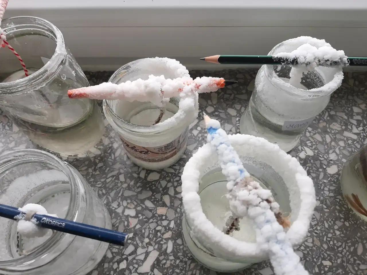 Słoiki z roztworem soli, w których rosną kryształy na ołówkach i sznurkach.