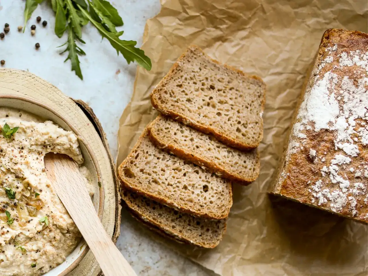 Chleb żytni, pokrojony w kromki, obok miski z pastą. Czy żyto ma gluten? Tak, żytnie pieczywo zawiera gluten.