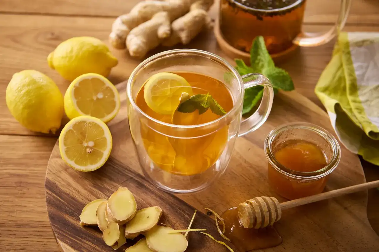 Herbata z imbirem i cytryną, plasterki cytryny, imbiru, miód i listki mięty na drewnianym blacie.