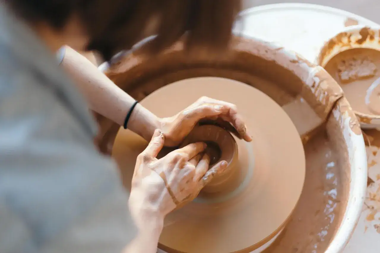 Dłonie artysty formują glinę na kole garncarskim. Powstaje piękna, ręcznie robiona pottery.