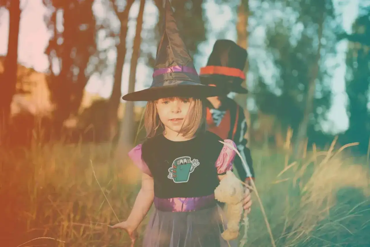 Dzieci w strojach z bajek, jakby z planu filmowego. Mała czarownica z pluszakiem i starszy kolega w kapeluszu.