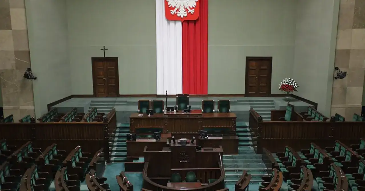 Pusta sala sejmowa z rzędami zielonych foteli i mównicą. Biało-czerwona flaga i godło Polski. Zastanawiasz się, ile jest posłów w sejmie?