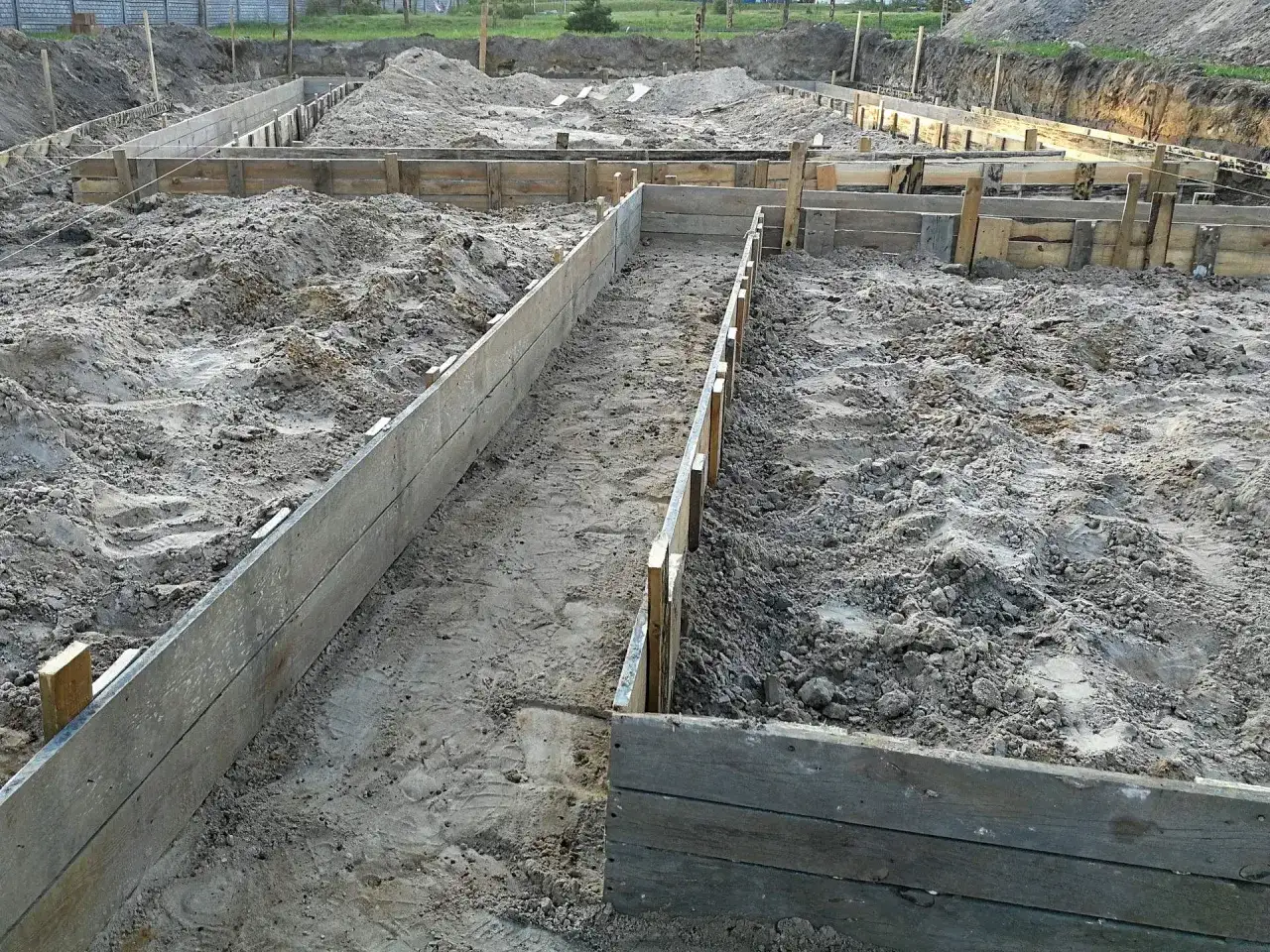 Wykonano wykopy pod fundamenty. Drewniane szalunki wyznaczają kształt przyszłego budynku na piaszczystym terenie budowy.