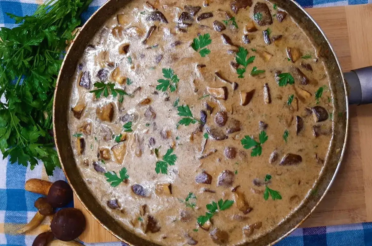 Kremowy sos grzybowy z natką pietruszki w patelni, obok świeże grzyby i natka.