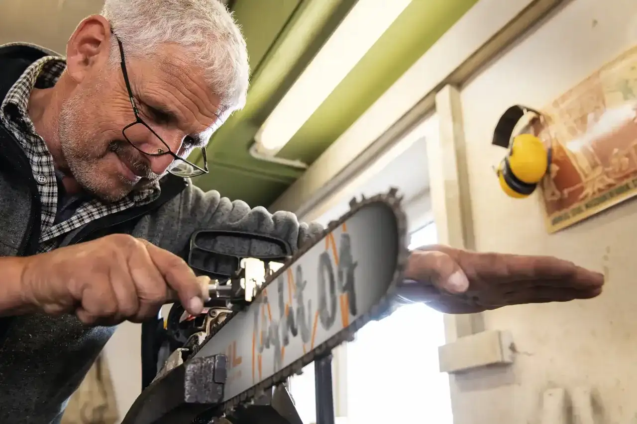Mężczyzna z okularami majstruje przy pile, pokazując, jak skrócić łańcuch do piły domowym sposobem.