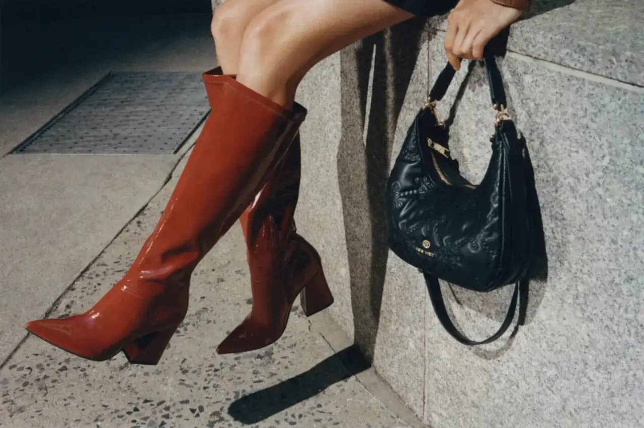 Kobieta w czerwonych kozakach i czarnej torebce z logo Nine West. Nine West to znana marka obuwia i akcesoriów.