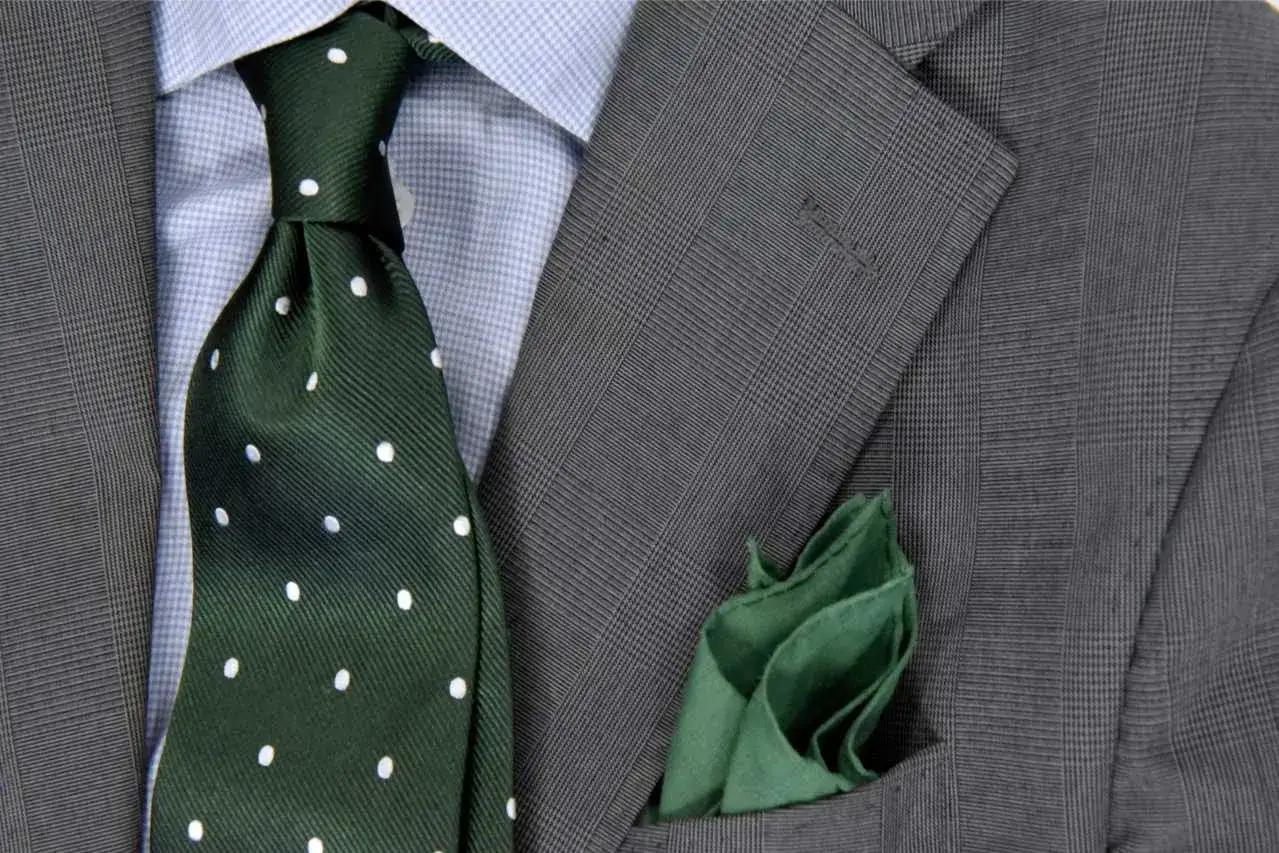 Szara marynarka w kratę, błękitna koszula, zielony krawat w kropki i zielona poszetka.