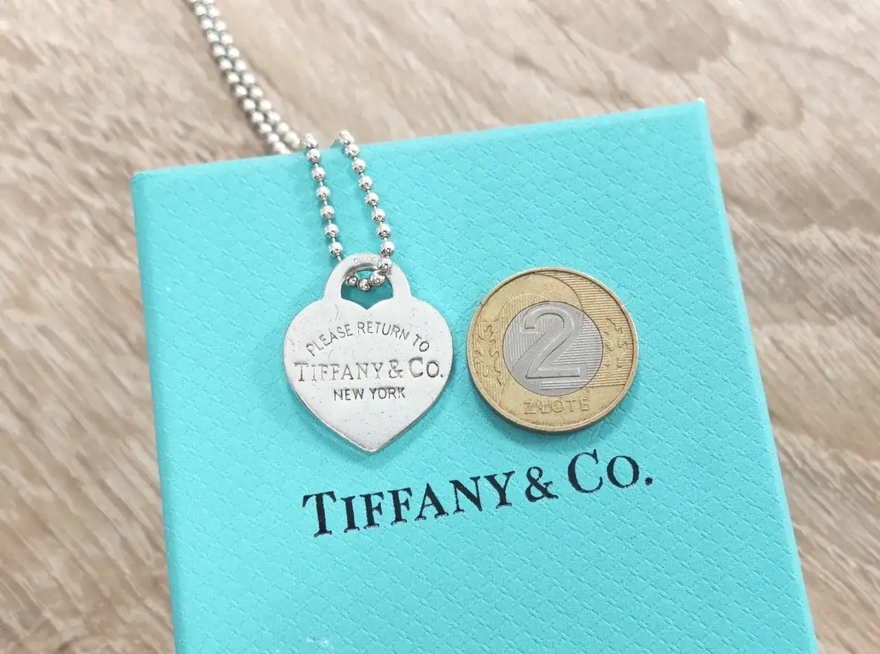 Srebrne serce z napisem "Please Return to Tiffany & Co. New York" na turkusowym pudełku Tiffany & Co. z monetą 2 złote.
